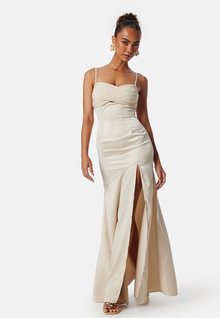 Beige satin aftonklänning med en åtsittande bodice, tvinnad halsringning, tunna axelband och en hög slits vid låret. Slät textur med flödande kjol.