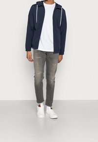 Navy hooded jacket with white drawstrings, layered over a white t-shirt. Worn with light gray distressed jeans and white sneakers.