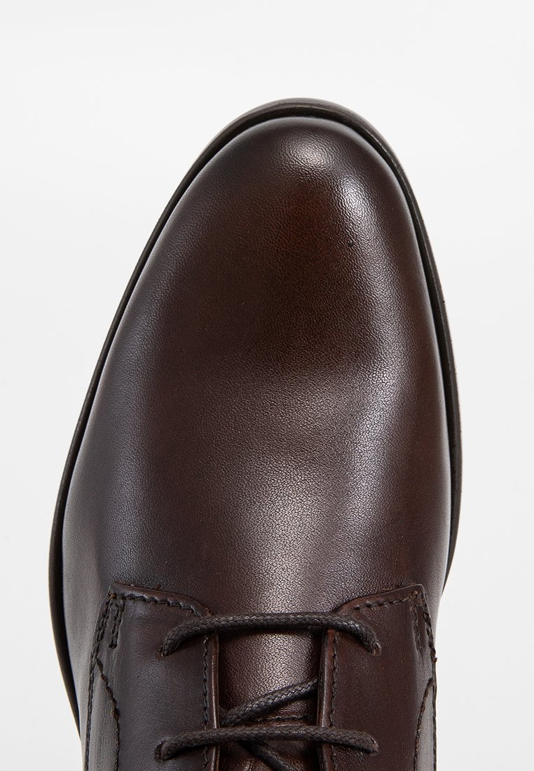 Zapato de cuero marrón con un acabado suave, punta redondeada y costuras en contraste en los laterales. Diseño clásico de cordones.