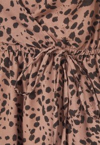 Hnědá tkanina s černým leopardím potiskem má v pase zavazování a nařasené detaily. Textura je měkká a lehká.
