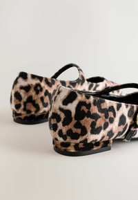 Chaussures de ballet imprimées léopard avec une texture douce et veloutée, bout arrondi et bord noir. Présente une petite sangle décorative sur chaque chaussure.