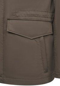 Khaki Außenjacke mit strukturierter Oberfläche, großer Klappentasche und gesteppten Akzenten. Das Material wirkt glatt und wasserabweisend.