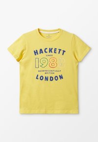 Żółta bawełniana koszulka z okrągłym dekoltem. Posiada napis "HACKETT od 1983 roku QUINTESSENTIALLY BRITISH LONDYN" w różnych kolorach.
