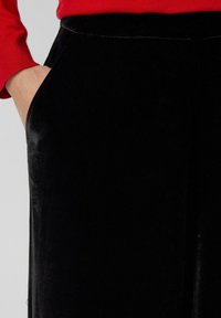 Zwarte fluwelen broek met een zijzak, uitgerust met een gladde textuur en een losse pasvorm, gecombineerd met een rode lange mouw top.