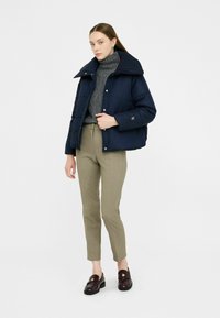 Granatowa puchówka z wysokim kołnierzem, noszona na szarym golfie. Połączona z beżowymi dopasowanymi spodniami i burgundowymi loafersami. Nowoczesny design.