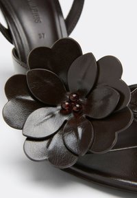 Sandale en cuir marron foncé avec une grande décoration florale superposée et trois petites perles brillantes au centre.