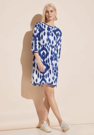 Blau-weißer, gemusterter Kleid mit Dreiviertelärmel, Taillenkordel, seitlichen Taschen und leichtem Stoff, getragen mit weißen Sneakers.
