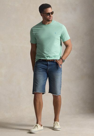 Μέντα πράσινη μπλούζα με στρογγυλή λαιμόκοψη, μπλε τζιν σορτς με ξεφτισμένα τελειώματα, καφέ ζώνη και κρεμ αθλητικά παπούτσια. Τα γυαλιά ηλίου ολοκληρώνουν την casual εμφάνιση.