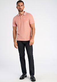 Ljusrosa kortärmad polo med vita detaljer, med en tvåknappsknäppning och strukturerad tyg, i kombination med smala svarta byxor och skor.