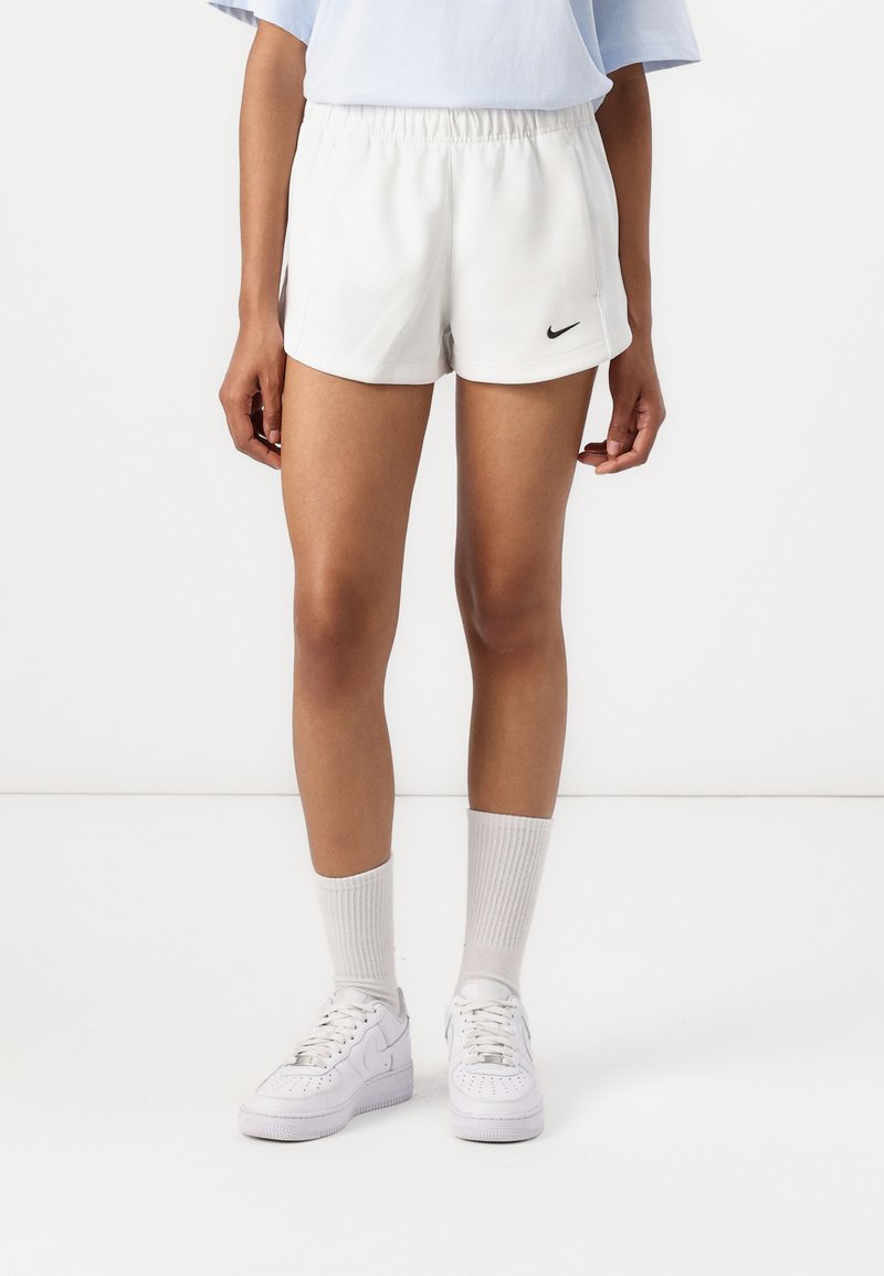 Balti sportiniai šortai su elastinga juosta, papuošti mažuoju juodu Nike logotipu. Sukomplektuoti su baltais batais ir iki kelių siekiančiomis veltinėmis kojinėmis.