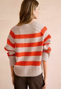 Stripet pullover-sweater i lys grå og orange med ribbet kant og brede ærmer. Har en bagsøm detalje og en afslappet pasform.