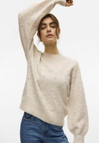 Maglione beige chiaro con pois testurizzati, scollatura rotonda e maniche lunghe a palloncino. Realizzato in morbido tessuto a maglia, con orlo a coste.