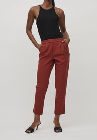 Body noir côtelé associé à un pantalon taille haute couleur rouille, cintré avec plis. Le mannequin porte des talons ouverts noirs.