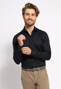Zwarte shirt met lange mouwen, een button-down kraag, een strakke pasvorm en een gladde textuur; gecombineerd met beige broek en een gevlochten riem.