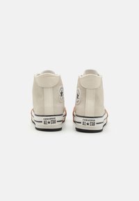 Baskets montantes en suede beige, avec un dos texturé, semelles en caoutchouc blanc, rayures noires et accents du logo Converse All Star.