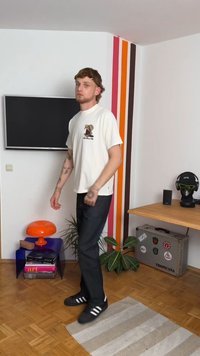 Camiseta branca com um gráfico, jeans escuros e sapatos pretos com listras brancas; o quarto apresenta uma parede listrada multicolorida e um chão de madeira.