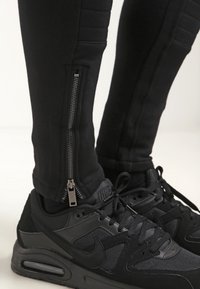 Svarta sportbyxor med dragkedja på sidan och texturerade paneler, i kombination med svarta Nike-sneakers med texturerad yta och snörningsdesign.