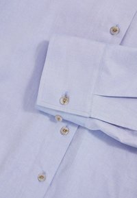 Light blue long-sleeve shirt with a smooth texture, featuring five tan buttons on the cuff and a folded sleeve.