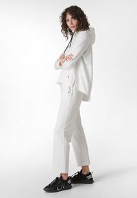 Sudadera blanca con cordones negros, combinada con pantalones blancos. Zapatillas negras con marca. Tejido suave, corte relajado y diseño minimalista.
