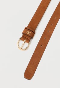 Tan leather belt featuring a gold metal buckle, smooth texture, with a logo accent on the strap and multiple adjustment holes.