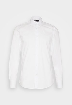 Camisa blanca de botones, hecha de algodón, con cuello clásico, mangas largas y dobladillo curvado. Diseño minimalista con sutiles detalles de costura.