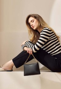 Sac en cuir noir avec une finition texturée et une bandoulière en chaîne dorée, associé à un pull rayé noir et blanc et à un pantalon noir.