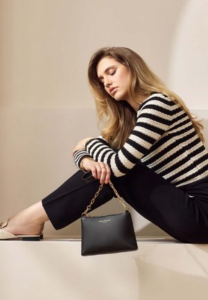 Sac en cuir noir avec une finition texturée et une bandoulière en chaîne dorée, associé à un pull rayé noir et blanc et à un pantalon noir.