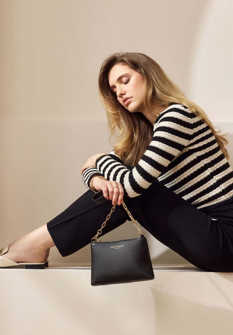 Sac en cuir noir avec une finition texturée et une bandoulière en chaîne dorée, associé à un pull rayé noir et blanc et à un pantalon noir.