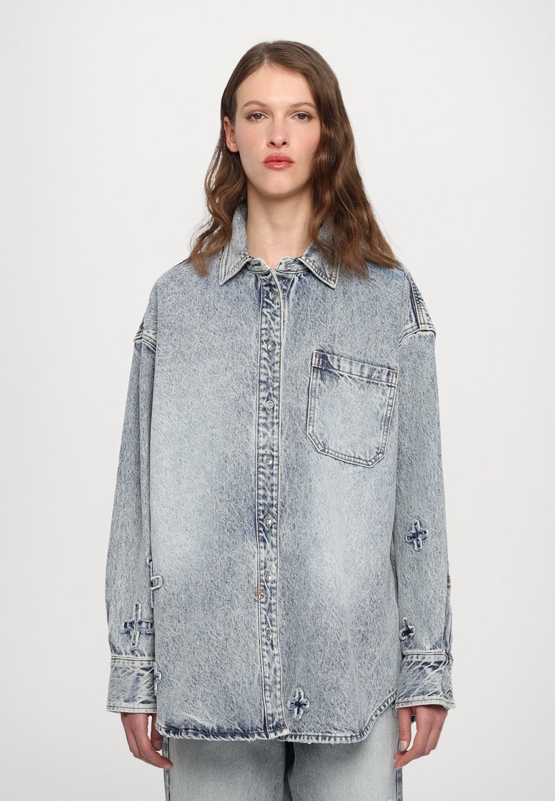 Šviesiai mėlynas džinsinis marškinis su mygtukų priekiu, krūtinės kišene, laisvu siluetu ir nusidėvėjimo detalėmis ant rankovių bei apvado.