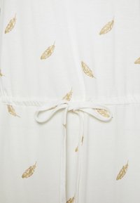 Vit tyg med guld fjädermönster, med en elastisk midja och en knytning i midjan.