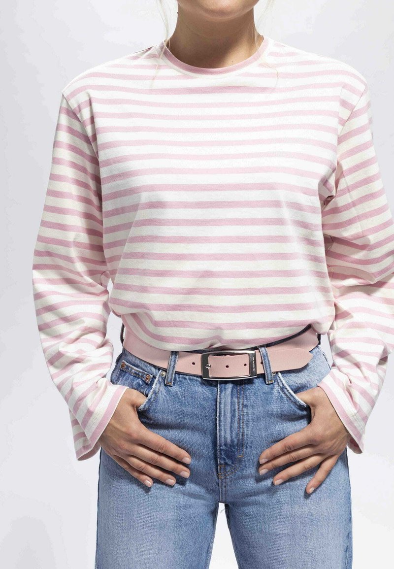 Camisa de rayas rosas y blancas de manga larga combinada con unos vaqueros de tiro alto azul y un cinturón rosa claro, mostrando un ajuste relajado y un diseño casual.