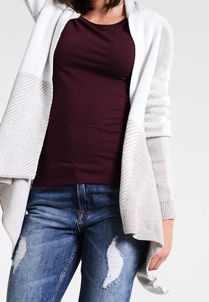 Gray and white patterned cardigan with an open front over a maroon top, paired with distressed blue jeans. Textured fabric and loose fit.