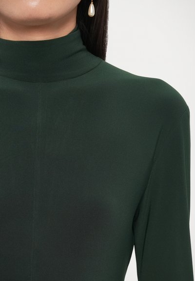 Blusa verde de cuello alto hecha de tela suave, con silueta ajustada y mangas largas. Detalle notable: brillo sutil y líneas de costura limpias.
