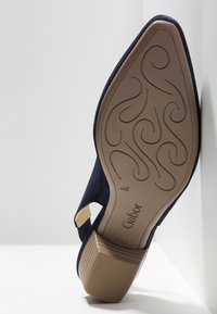 Chaussure en daim bleu marine à bout arrondi et bride ajustable, dotée d'une semelle en caoutchouc beige texturée avec un motif dessiné. Marque : Gabor.