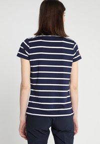 Chemise à manches courtes bleu marine avec des rayures horizontales blanches. Tissu doux avec un col rond, peu de détails sur la manche droite.
