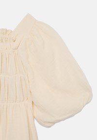 Blusa color crema con maniche corte a palloncino, corpetto smock e tessuto leggero e testurizzato.