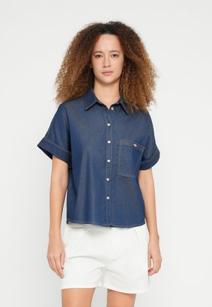 Marineblå denim kortermet skjorte med knappelukking foran, brystlomme og oppbrettede mansjetter. Jevn tekstur med synlige sømdetaljer.