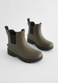 Bottes en caoutchouc vert olive à chevilles avec des côtés élastiques noirs, une semelle texturée pour l'adhérence et des languettes pour un enfilage facile. Fini lisse et imperméable.