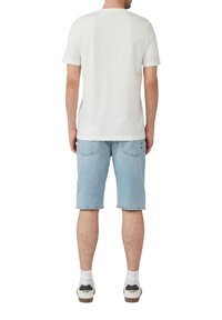 Witte katoenen T-shirt met korte mouwen, gecombineerd met lichtblauwe denim shorts. De korte shorts hebben achterzakken. Draagt het met witte sokken en sneakers.