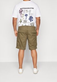 Vit t-shirt med svampillustrationer i olika färger; olivgröna cargoshorts; vita sneakers. Bakifrån, avslappnad passform; enkelt mönster.