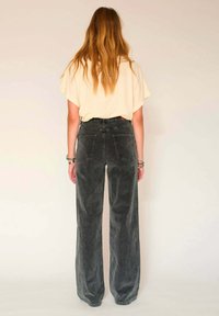 Pantalons en velours côtelé gris, à taille haute et à large jambe, avec des poches arrière, associés à un top beige ample. Détails de couture et texture visibles.