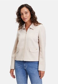 Ljust beige mockapälsjacka med krage, främre dragkedja och två ficklock. Slät textur och skräddarsydd design med långa ärmar.