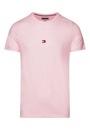 Jasnoróżowy t-shirt z krótkim rękawem i okrągłym dekoltem z wyszywanym napisem "Tommy Hilfiger EST. 1985" oraz małym logo marki na lewym rękawie.
