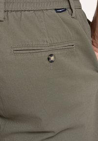 Męskie spodnie w oliwkowym kolorze wykonane z mieszanki bawełny. Posiadają tylną kieszeń z zapięciem na guzik oraz delikatnie teksturowaną powierzchnię.