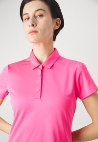 Lyserød polo shirt lavet af glat, strækbart materiale med spidse krave, korte ærmer og en seks-knap stolpe.