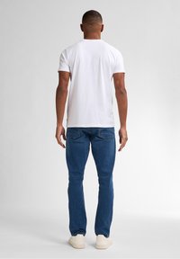 T-shirt bianca di cotone, maniche corte, scollo arrotondato, abbinata a jeans denim blu, design slim-fit, indossata con scarpe color crema.