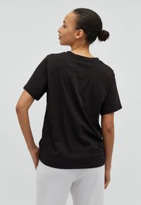 Zwarte katoenen t-shirt met een relaxte pasvorm, korte mouwen en een ronde halslijn, van achteren getoond, gecombineerd met lichtgekleurde broek.
