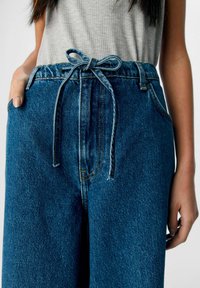 Hoge taille, wijde blauwe denim broek met een koordsluiting, voorzien van voorkruiden en contrasterende stiksels op de naden.