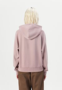 Hettegenser i myk rosa stoff, med ribbestrikkede ermer og nederkant, i avslappet passform og med stor baklomme.