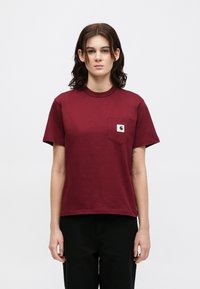 T-shirt in cotone bordeaux con colletto rotondo, maniche corte e taschino sul lato sinistro del petto con un piccolo etichetta del logo. Texture liscia.